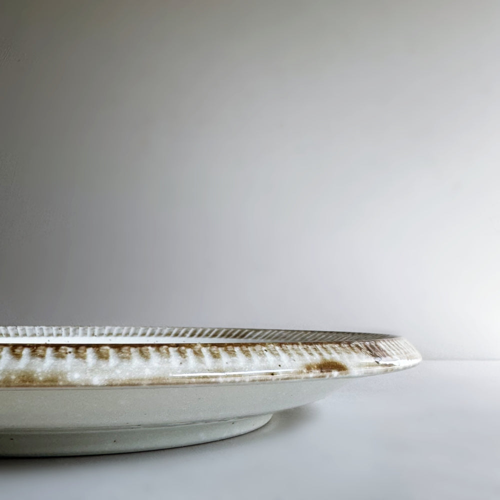 Raised rim dinner plate in cream white glaze. Fuchisabi Kohiki Plate made in Gifu prefecture, Japan. Mino Ware. Available at Toka Ceramics.