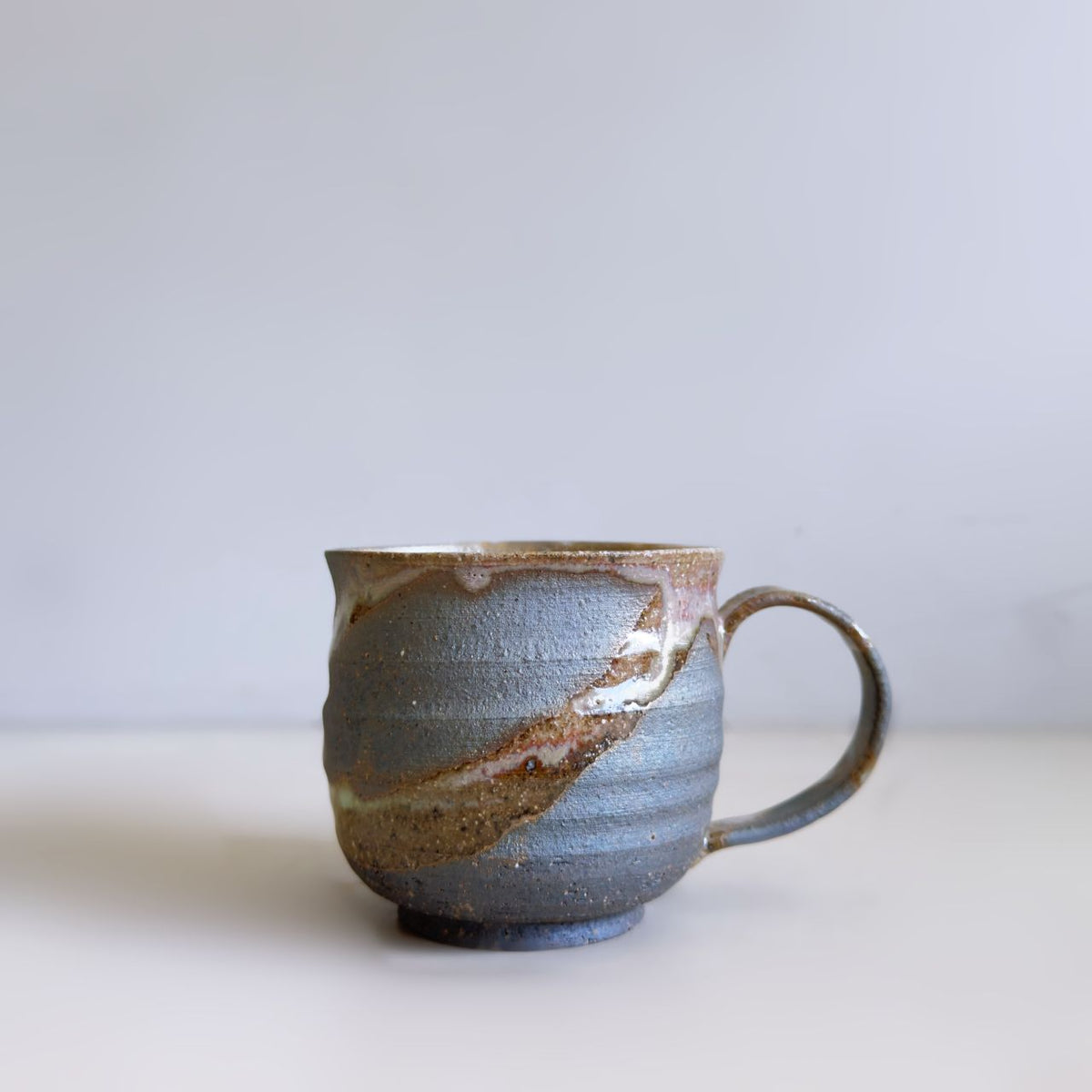 A handmade ceramic mug with a textured, ribbed surface, featuring a dark brown glaze with a diagonal brown and gold crackled pattern, set against a plain light grey background.