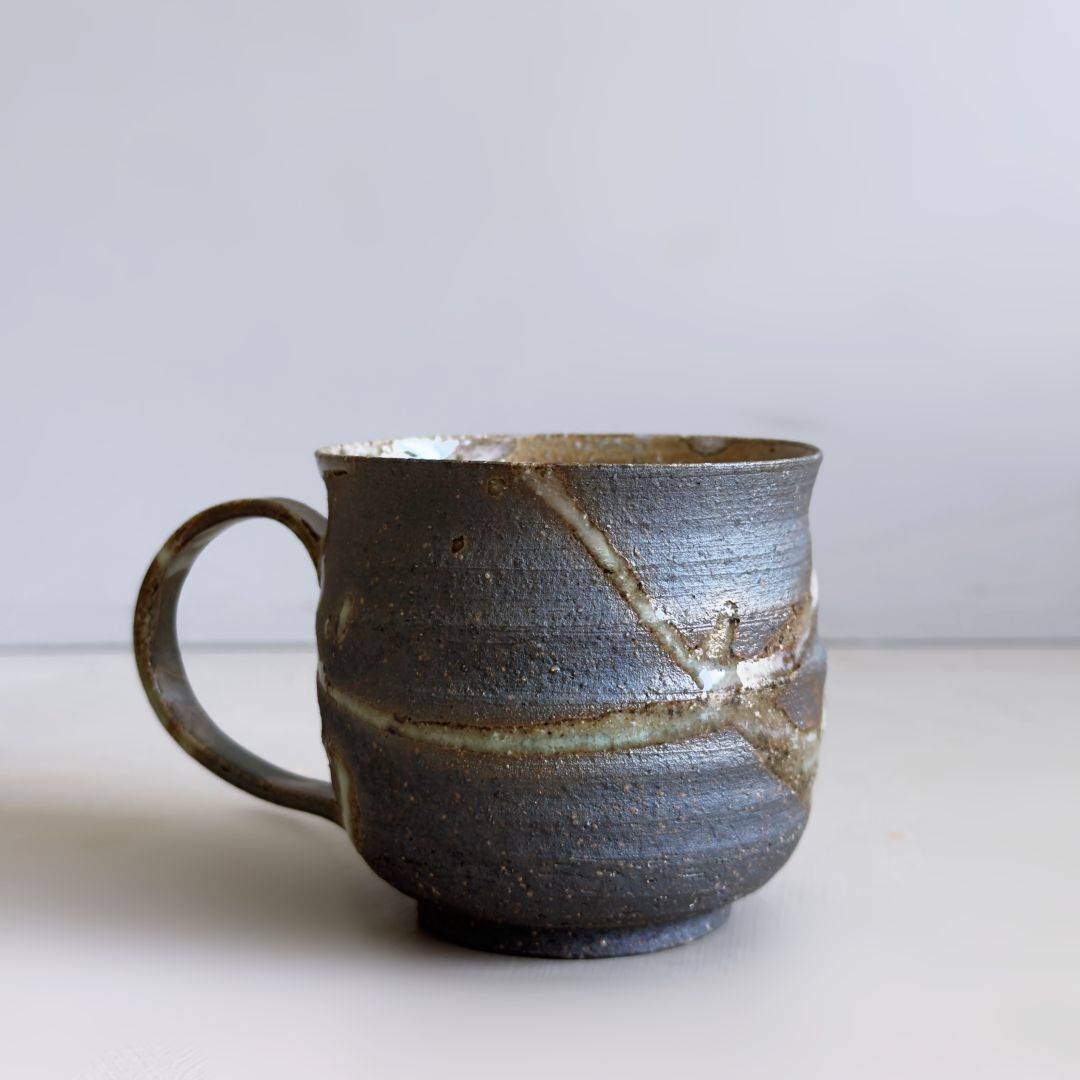 Front view of a dark Kisenyou ceramic mug with pale flowing glaze and curved handle at Senju Living