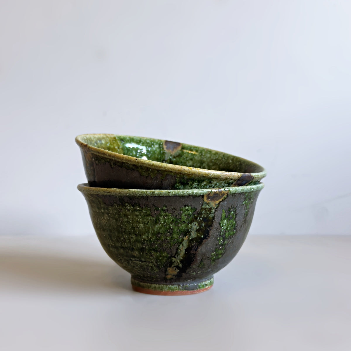 Two stacked Japanese ceramic rice bowls with a textured green oribe glaze, set against a plain light grey background.