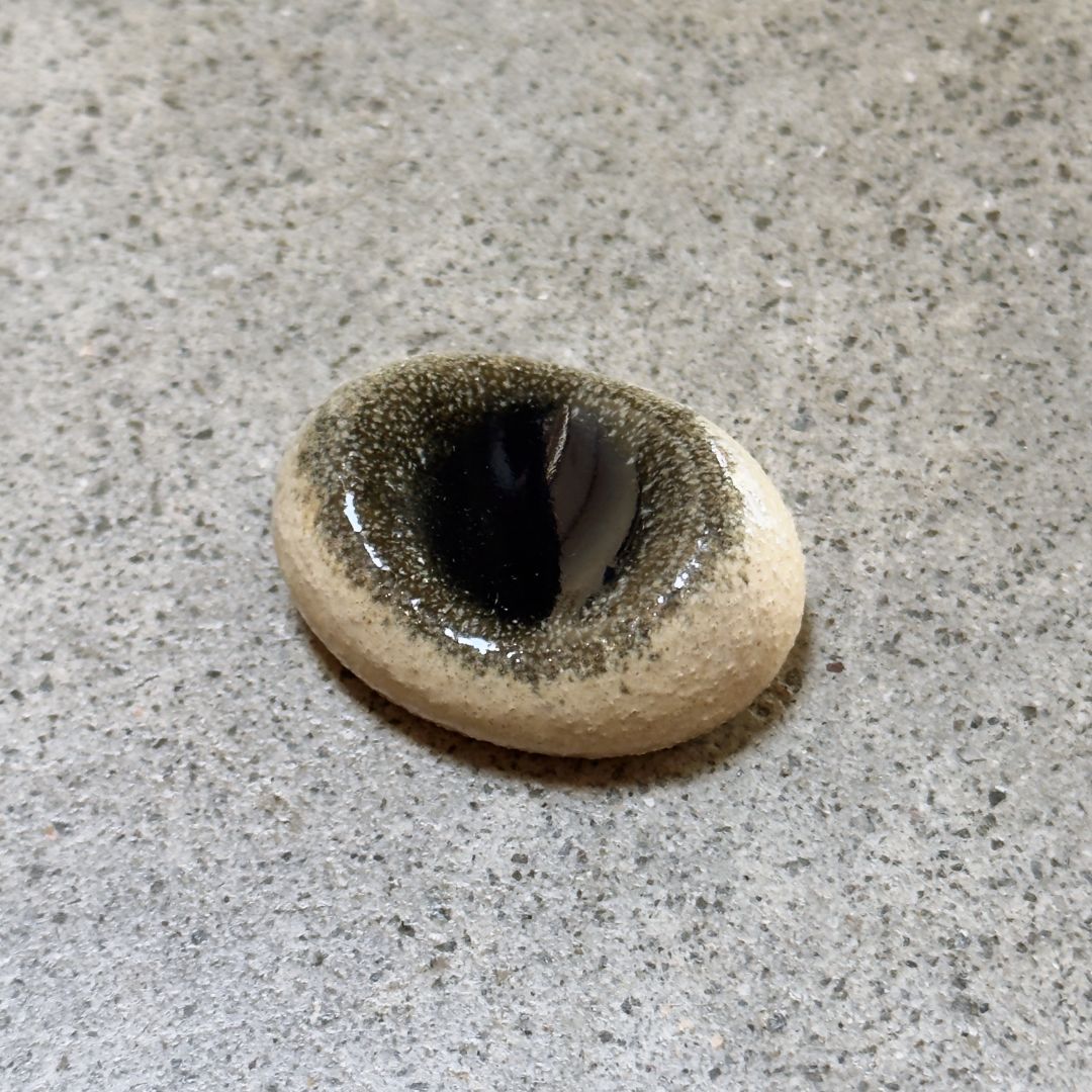 An oval Japanese ceramic chopstick rest with a dark centre, resting on a textured grey stone surface.