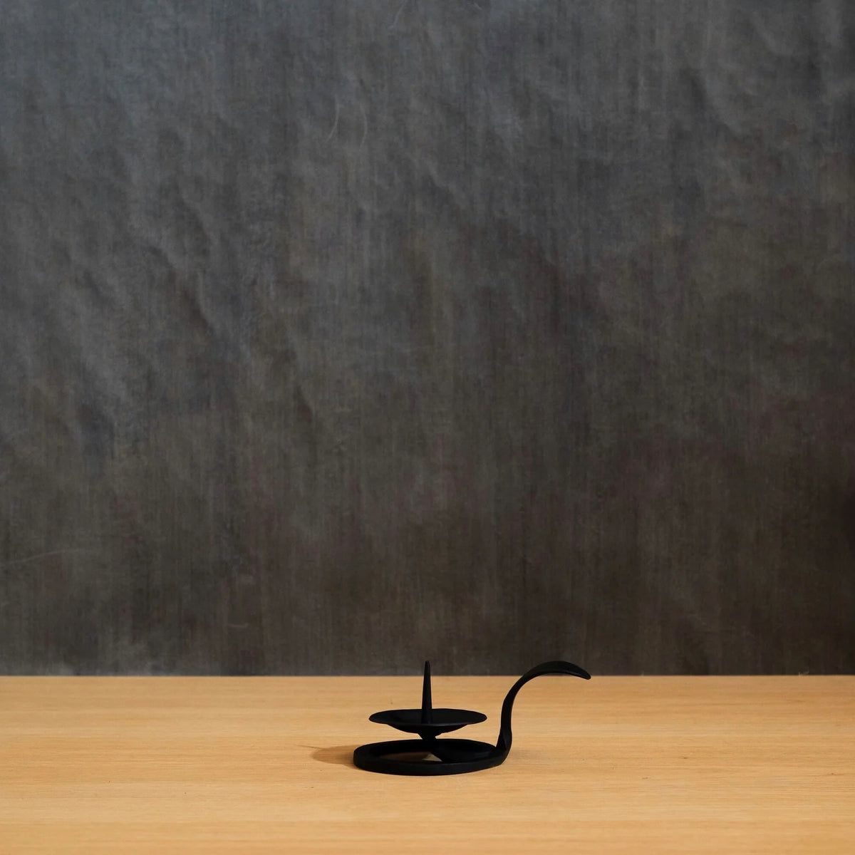 Japanese Iron Candle Holder set against dark textured wall on a wooden bench top
