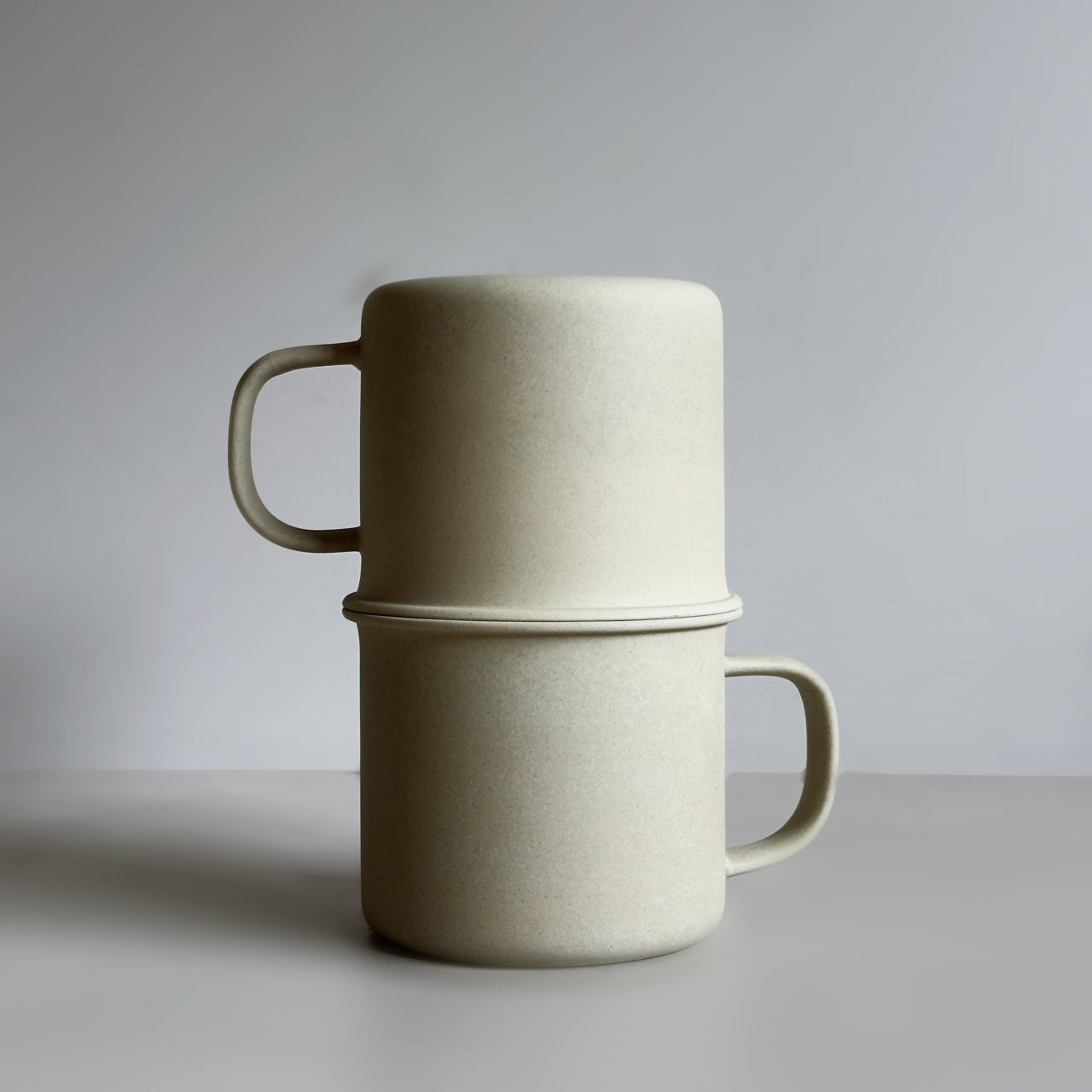 Two beige ceramic mugs stacked on a light gray background