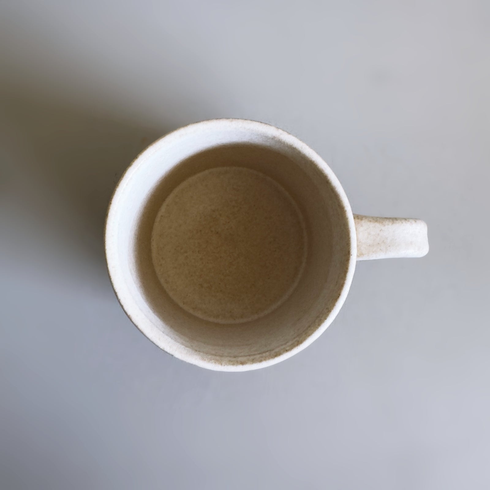 Top view of a Japanese Mino ware beige ceramic mug on a light grey background.
