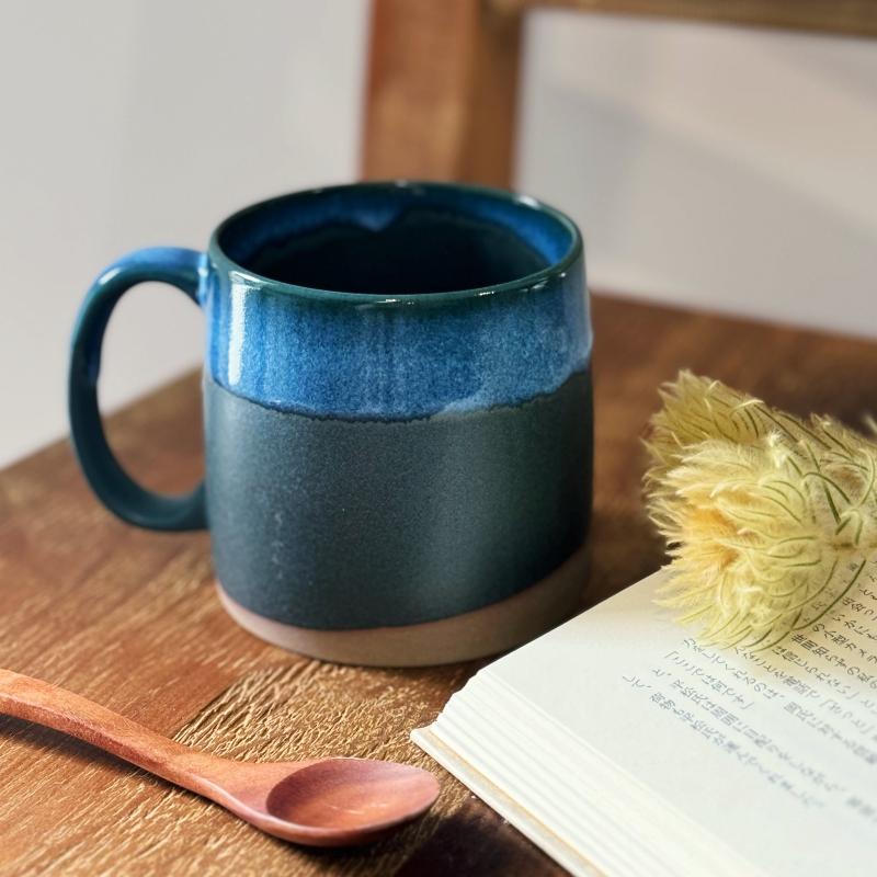 Dark blue Japanese TOKA ceramic mug and wooden spoon beside an open Japanese book, warm minimalist Japandi styling.