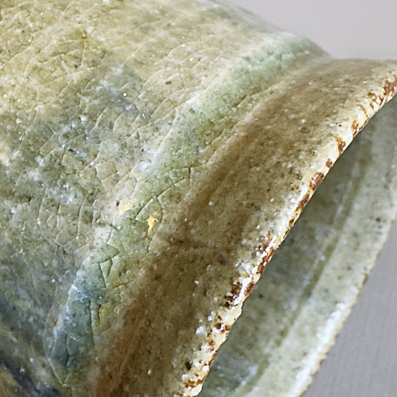 Close-up of a handmade Japanese ceramic cup showing a textured glaze with a mix of sage green, olive, and earthy brown tones.
