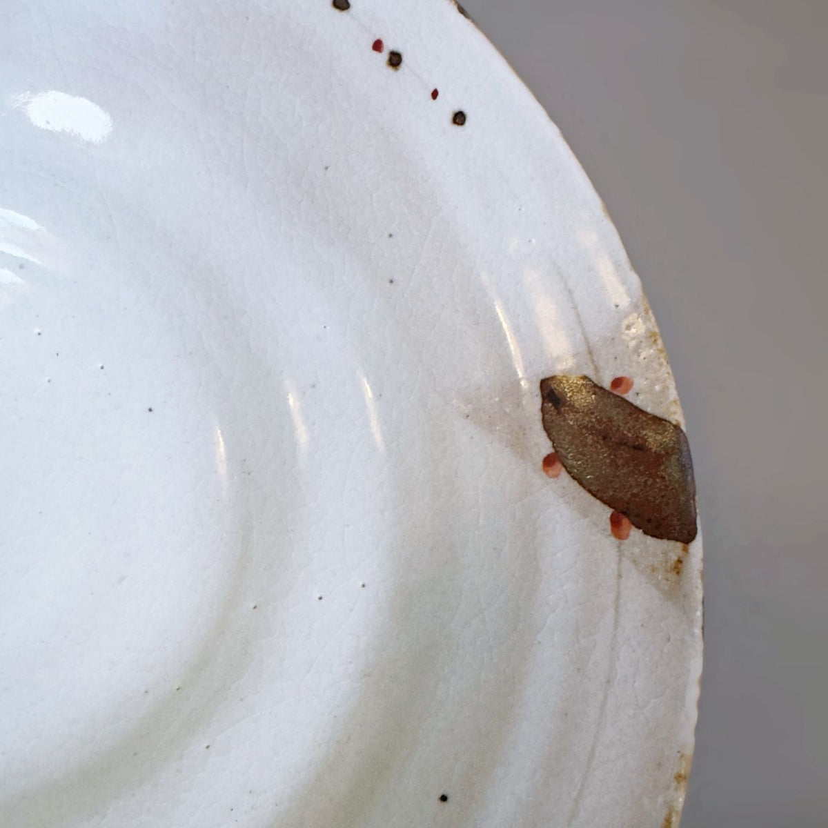 A close-up of a Japanese off-white ceramic bowl interior with a small brown stroke near the rim, against a neutral grey background.