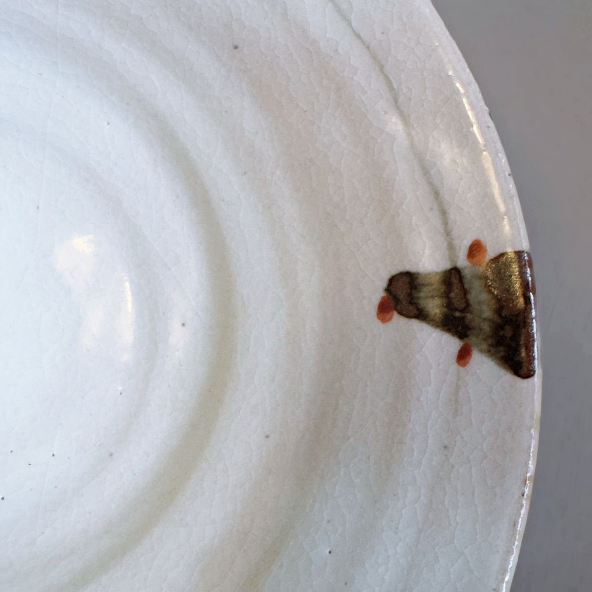 A close-up of a Japanese off-white ceramic bowl interior with a small brown stroke near the rim, against a neutral grey background.