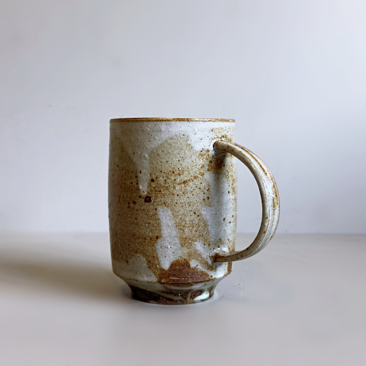 A handmade ceramic jug with a curved handle and warm cream-brown glaze, shown at a slight angle.