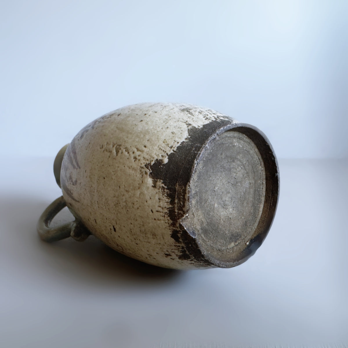 A vintage ceramic vase with a textured, speckled beige and brown glaze, shown from its open base on a light grey background.