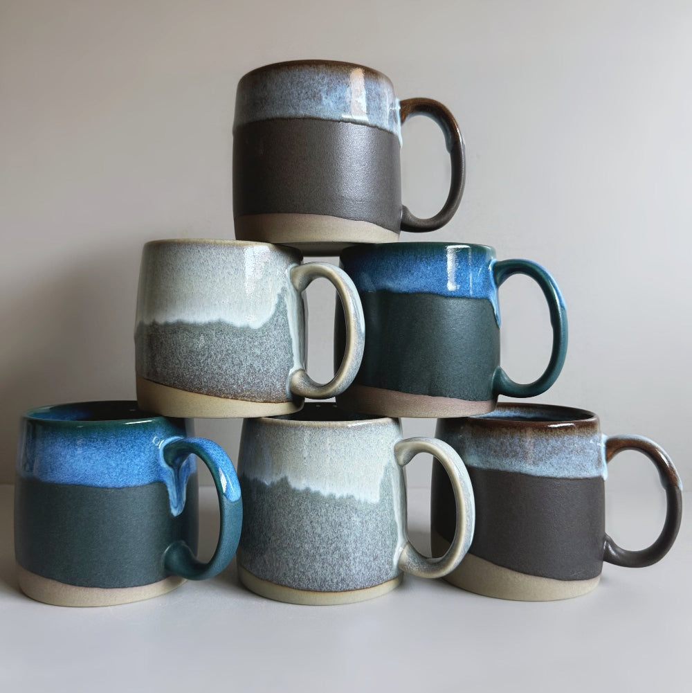 Stack of ceramic mugs with various color patterns on a plain background