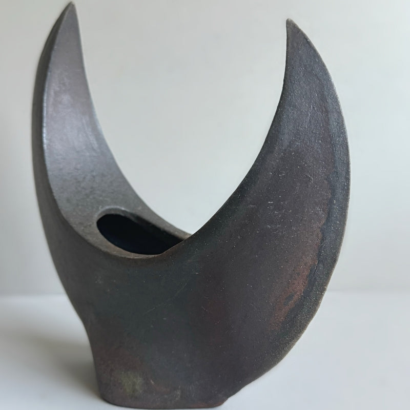 A handcrafted Crescent Vase made by Tsugaru Kanayama Pottery in Japan, featuring a unique crescent moon shape and dark earthy tones.