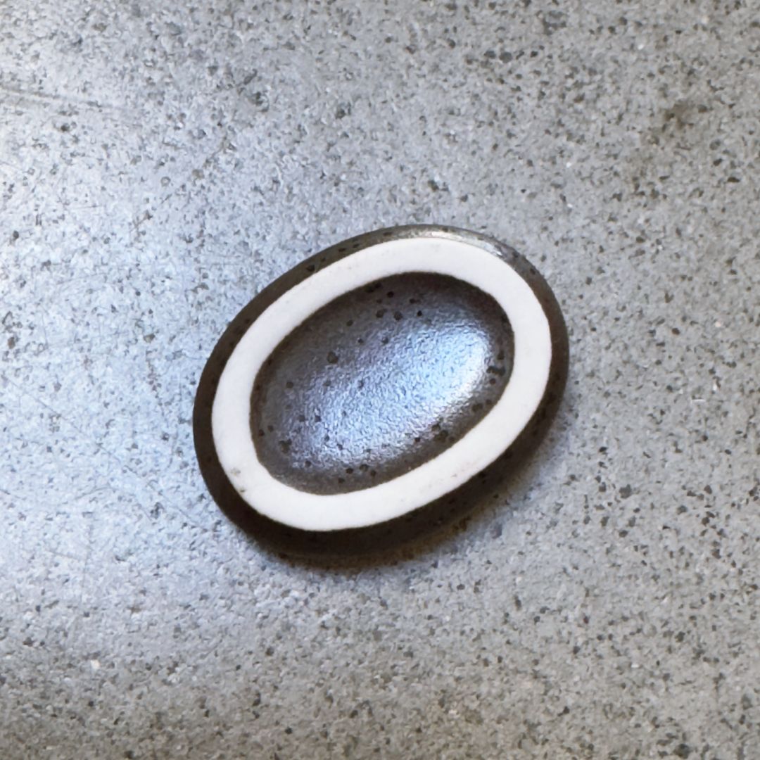 A bottom view of an oval ceramic chopstick rest with a dark brown speckled glaze, shown on a grey concrete surface.