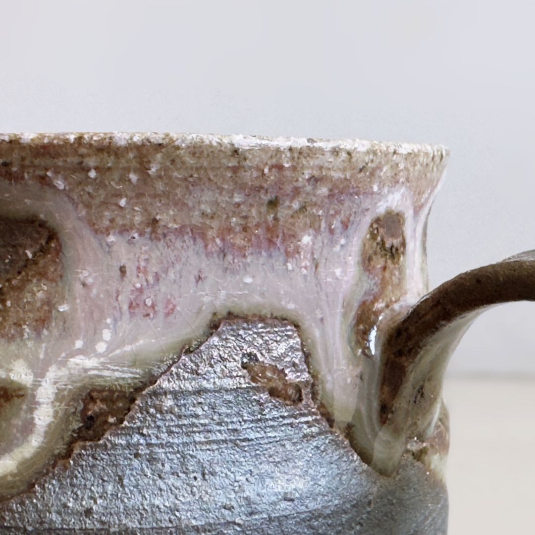 Close-up of layered cream and pink glaze beside the mug handle against a pale grey background.