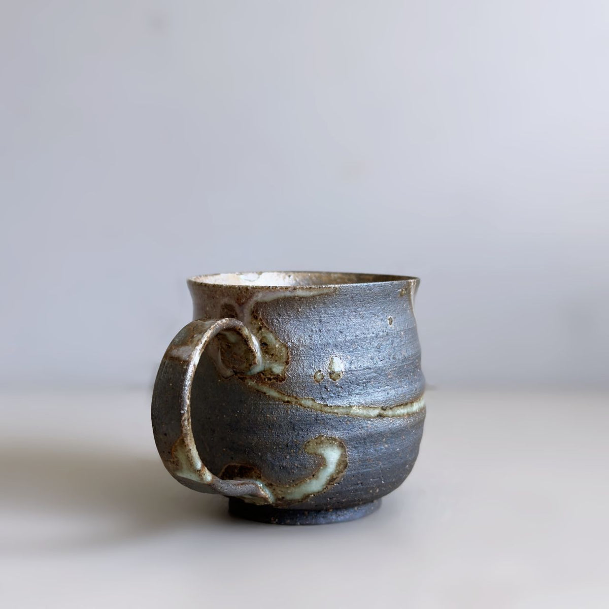Reverse view of Kisenyou mug with curved handle and flowing glaze detail against a pale grey background.