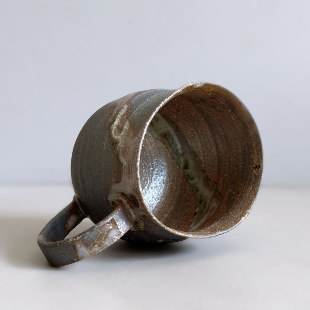 Angled view of the Kisenyou mug showing its earthy interior and curved handle on a pale grey background.