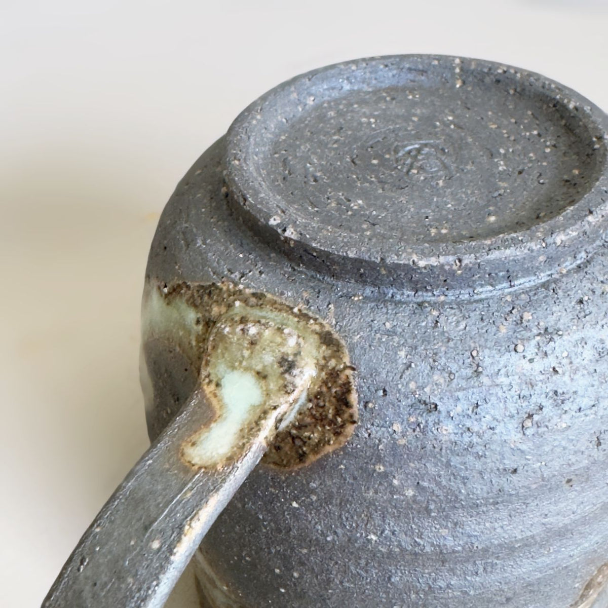 Close-up of the lower handle join and speckled dark clay against a pale grey background.