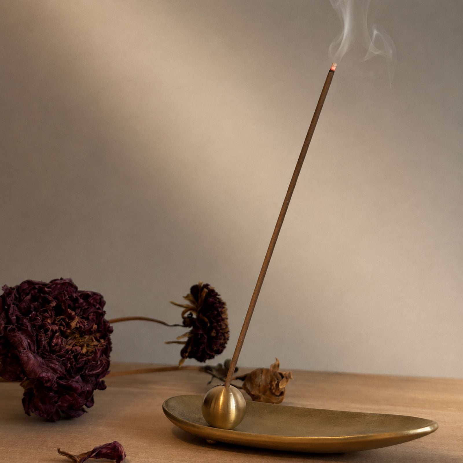 Lit Japanese incense stick by Kousaido gently smoking in a brass holder on a wooden table, minimalist Wabi-sabi home decor.