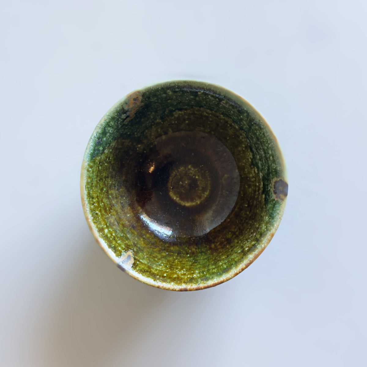 A Japanese handmade ceramic rice bowl viewed from directly above, featuring a glossy oribe glaze that transitions from olive green on the rim to a deep dark brown in the centre.