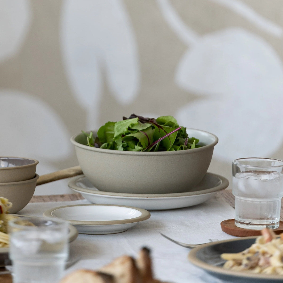 Dining table with a bowl of salad, bread, and glasses on a neutral background