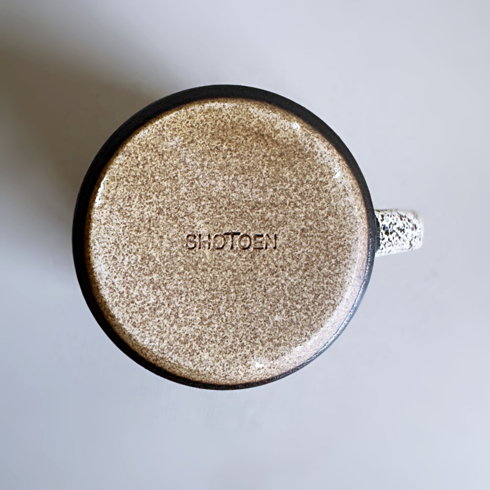 Top view of a bottom of glittery mug with 'SHOTOEN' stamp on a light grey background.