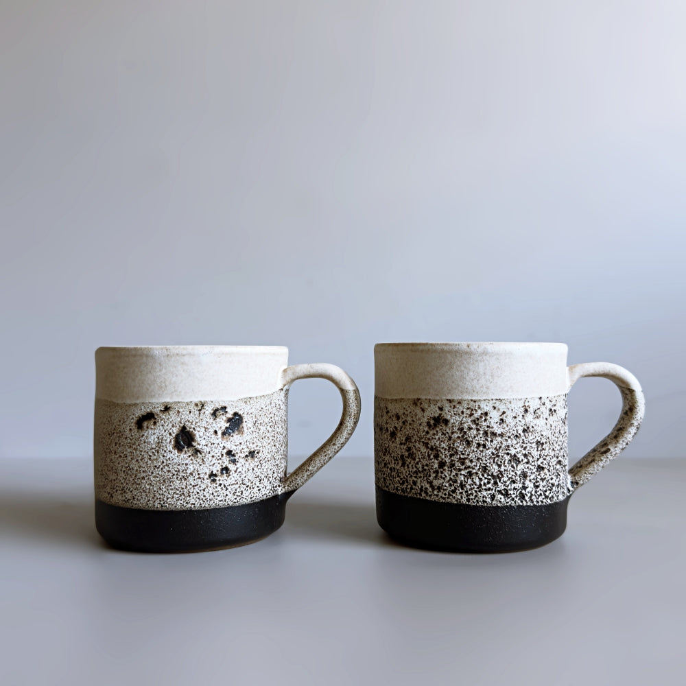 Front view of two Japanese Mino ware ceramic mugs with speckled design on a plain background.