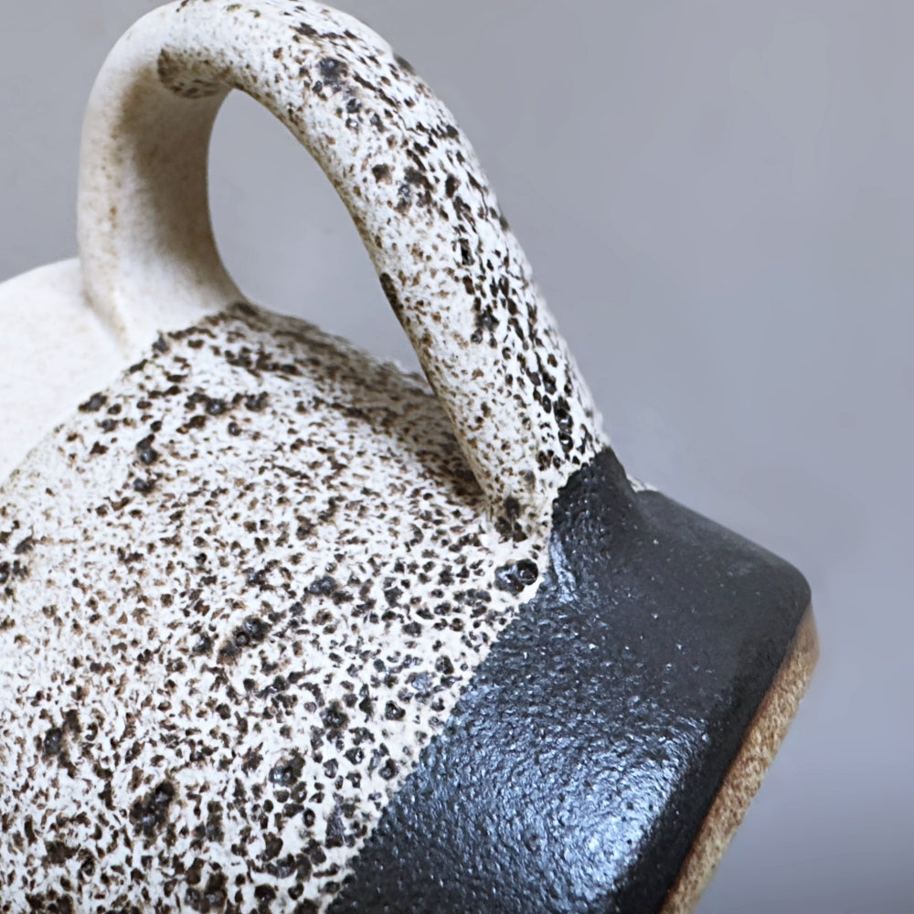 Close-up of a Japanese Mino ware ceramic mug with speckled glaze and black accent on a grey background.