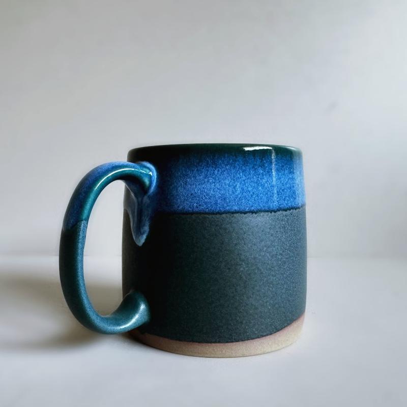 Detail of a dark blue TOKA ceramic mug showing a vibrant blue dripping glaze over the large loop handle.