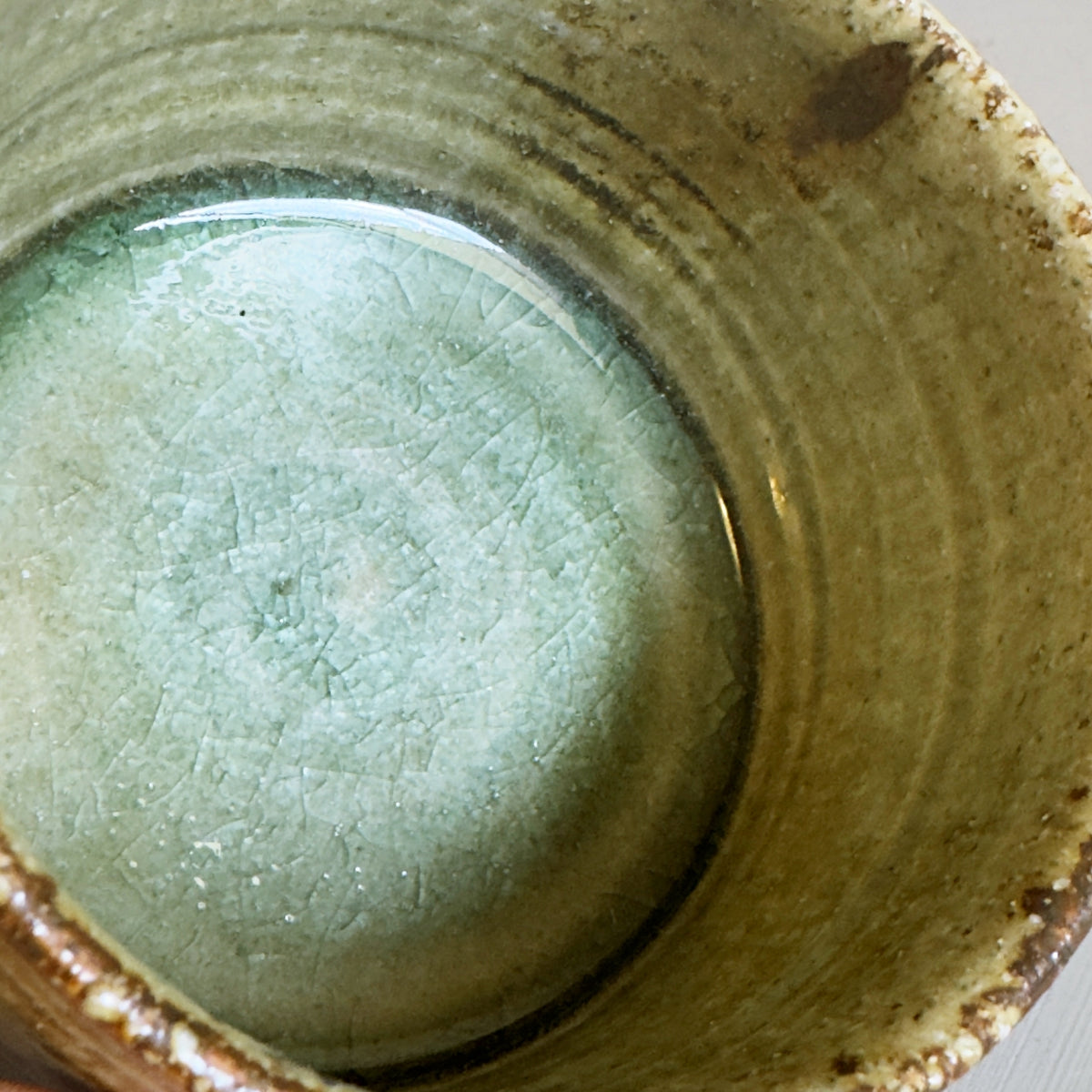 Close-up of a handmade ceramic Japanese matcha bowl with a textured interior glaze in pale mint green  at the bottom and earthy brown tones.