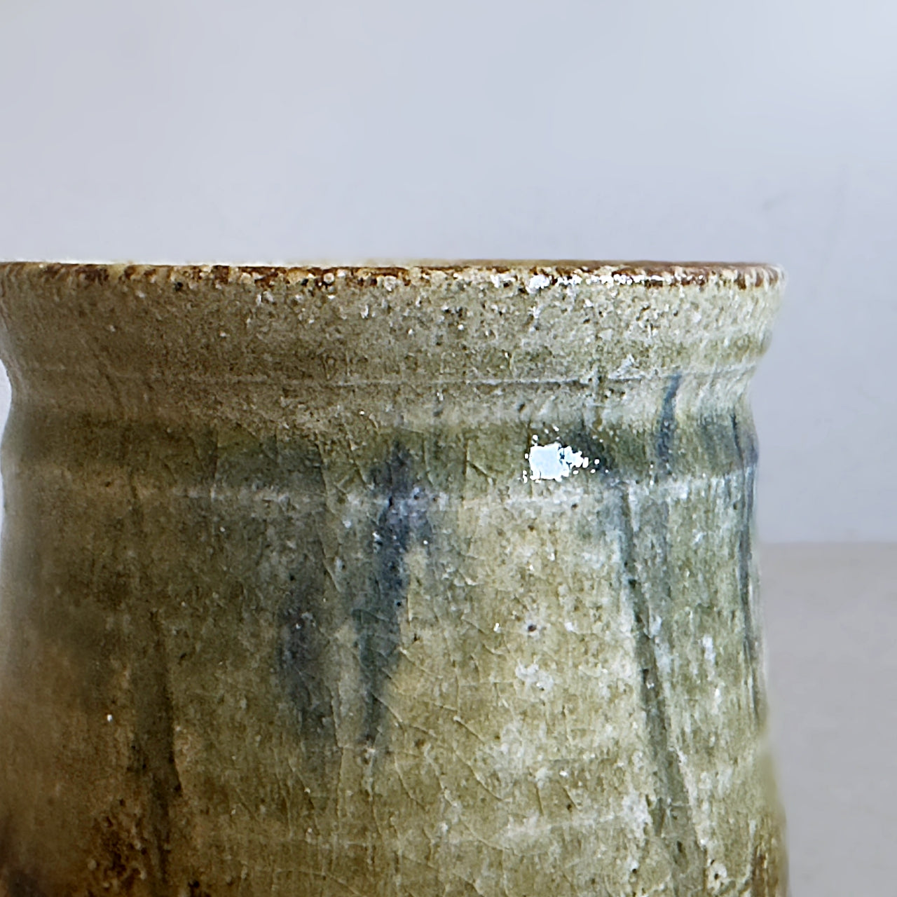 Close-up of a handmade Japanese ceramic tea cup with a rustic glaze in earthy green, beige, and brown tones.
