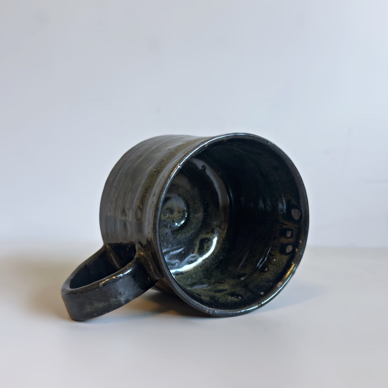 Angled view of a black handcrafted Minoware ceramic mug resting slightly on its side, at Senju Living.