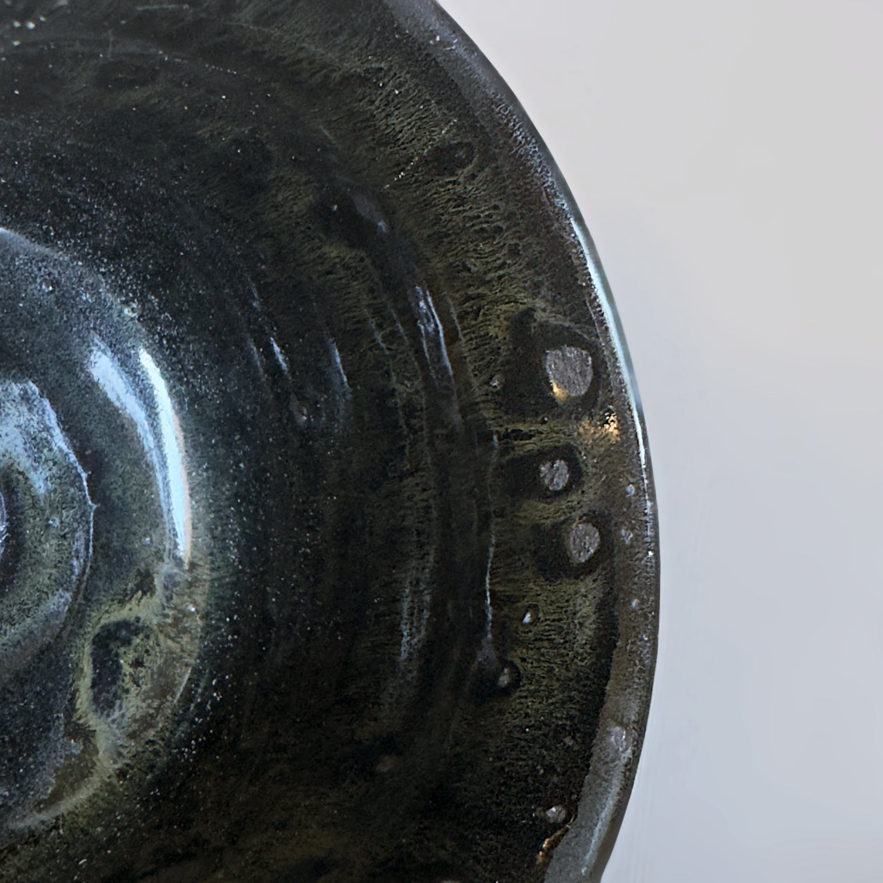 Macro detail of the dark, iridescent glaze and organic textures inside a black Minoware mug, from Senju Living.