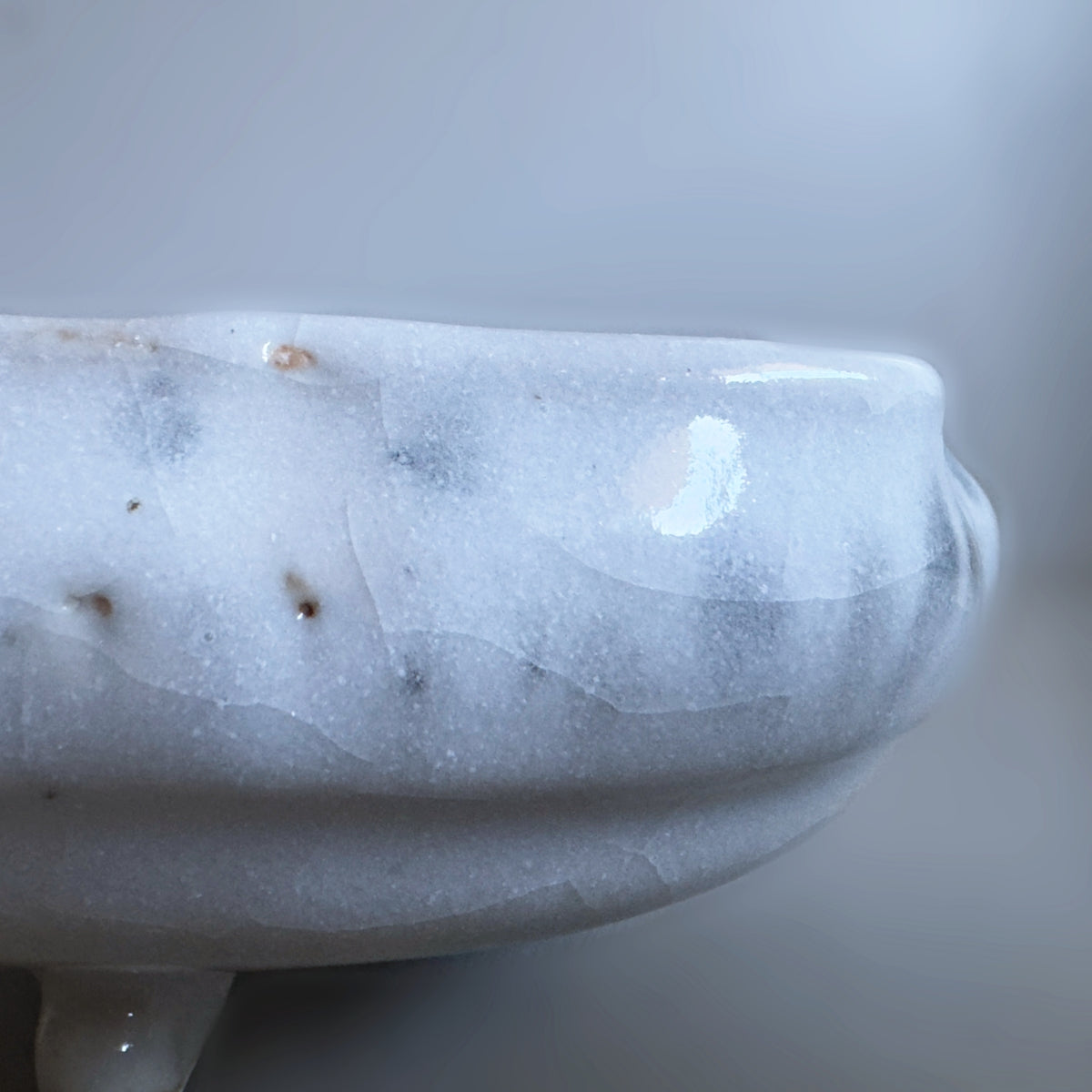 A close-up of a glossy white Japanese ceramic bowl with subtle grey marbling and small natural inclusions, set against a soft grey background.