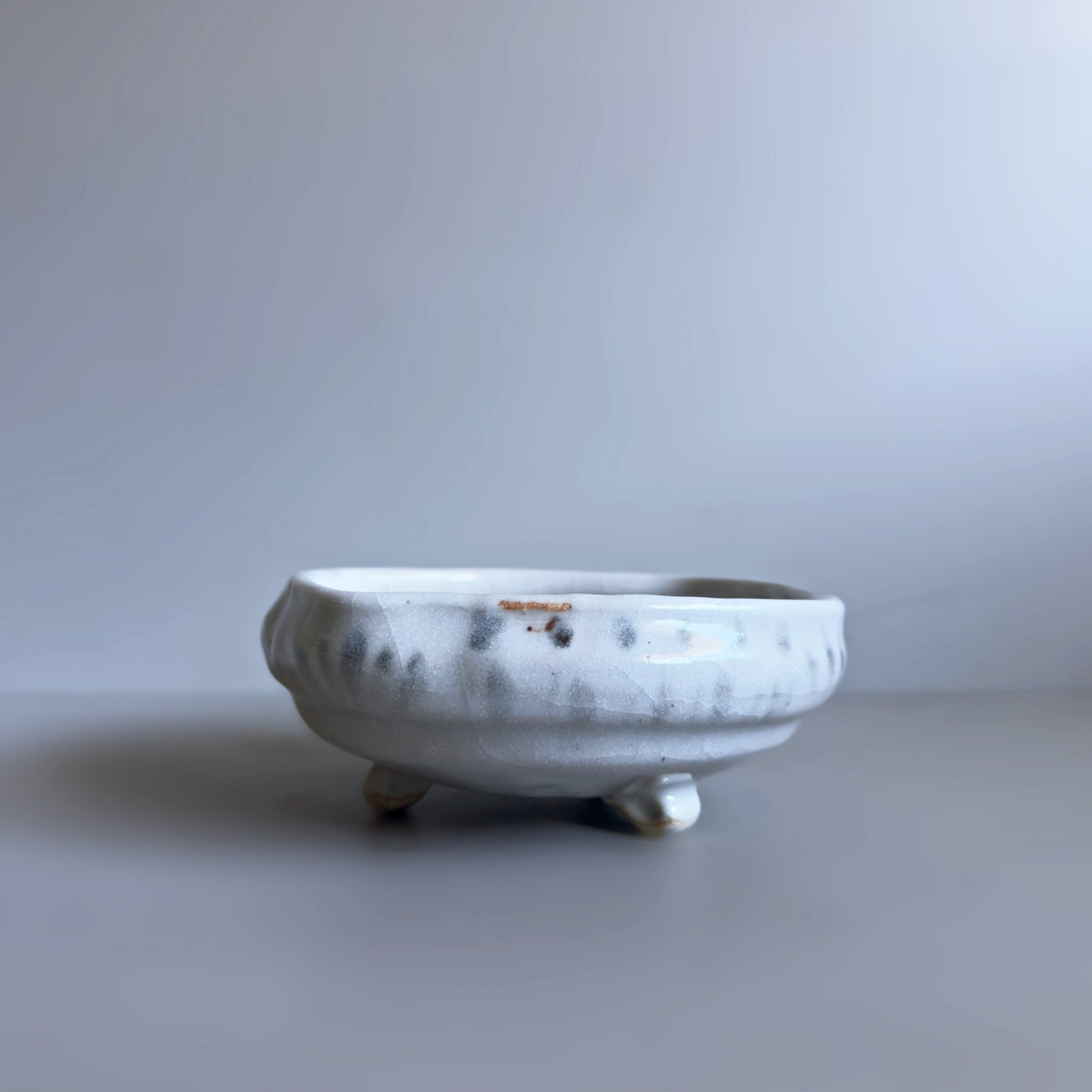 A square Japanese ceramic footed bowl with a speckled white and grey glaze, photographed on a neutral grey background.