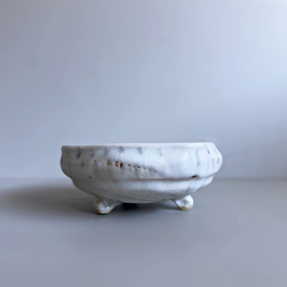 A square Japanese ceramic footed bowl with a speckled white and grey glaze, photographed on a neutral grey background.